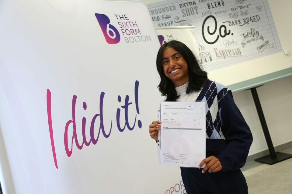 A student holding up results paper and smiling
