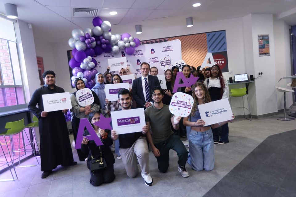 A group of people is celebrating with signs and balloons indoors, appearing to be part of a joyful event.